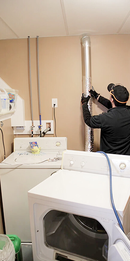Technician cleaning dryer vent ductwork in laundry room with specialized equipment